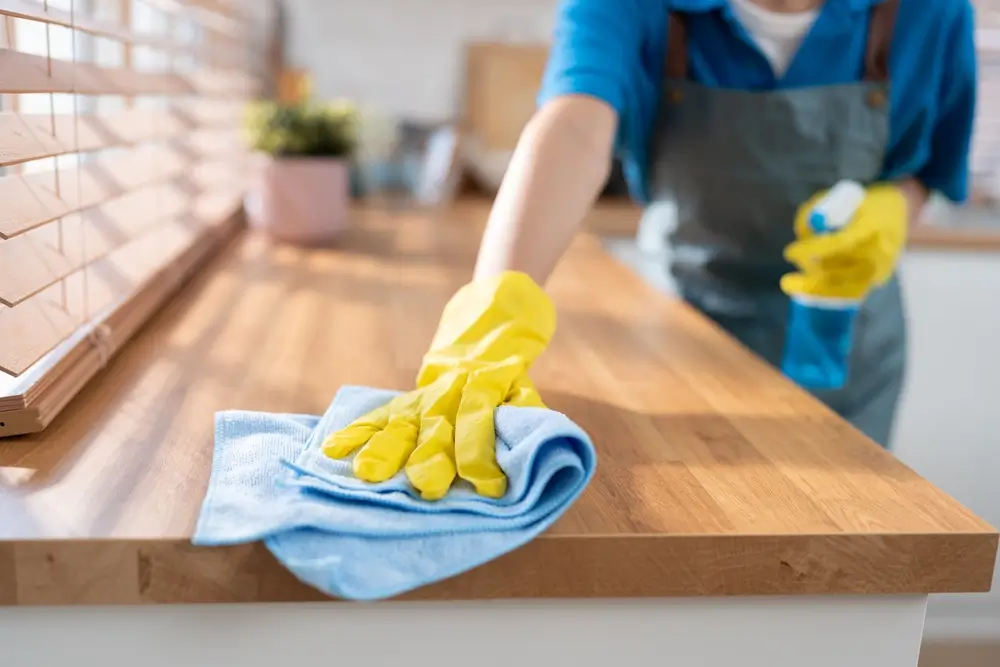 Porządek w kuchni. Sprzątanie kuchni przez panią, która ma na rękach żółte rękawiczki i trzyma niebieską ściereczkę.