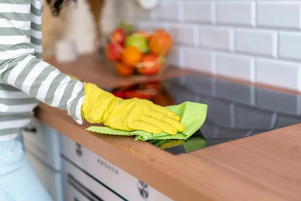 Kobieca ręka w żółtej rękawiczce, czyszcząca płytę indukcyjną przy pomocy ściereczki. Jak czyścić płytę indukcyjną?